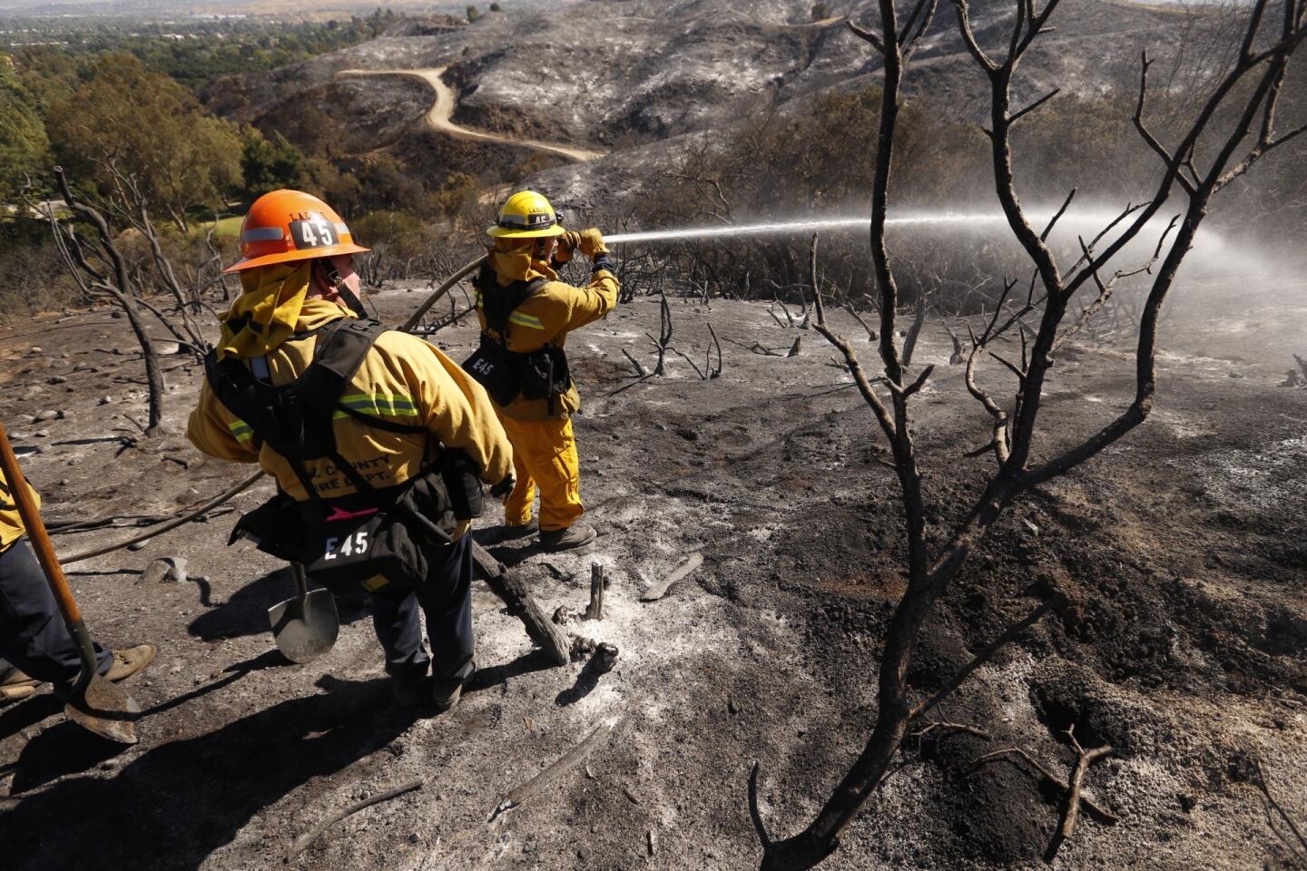 LA County Fire Engineer Todd Jameson and Captain Ritchie Salisbury, left, water down hot spots on the burned hillside of the Hidden Valley neighborhood in Santa Clarita Thursday morning.