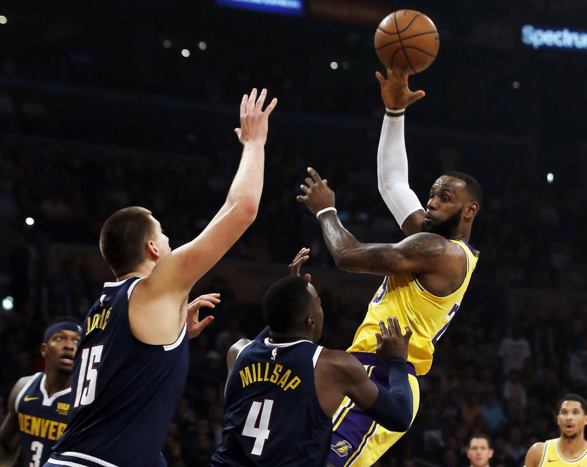 El jugador de los Lakers de Los Ángeles LeBron James (derecha), pasa la pelota sobre sus rivales de los Nuggets de Denver Nikola Jokic (15) y Paul Millsap (4) en la primera mitad del juego de la NBA que enfrentó a ambos equipos en Los Ángeles, el 25 de octubre de 2018.