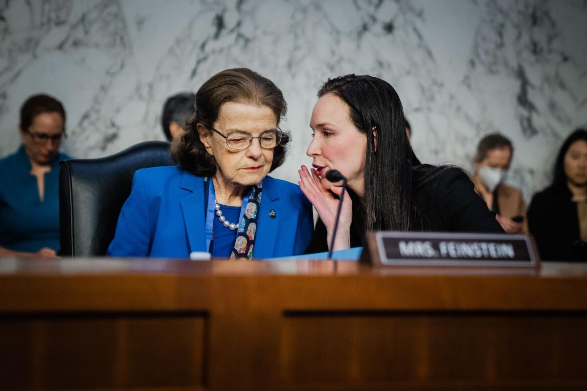 Dianne Feinstein listens in as her aide speaks to her ear during a hearing at the senate chamber
