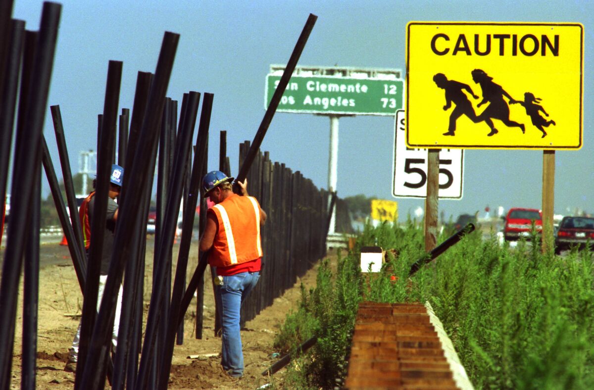 Contractors in 1993 set posts for an 8-foot fence in the median of the 5 Freeway in the shadow of an iconic yellow pedestrian warning sign. (Don Bartletti / Los Angeles Times)