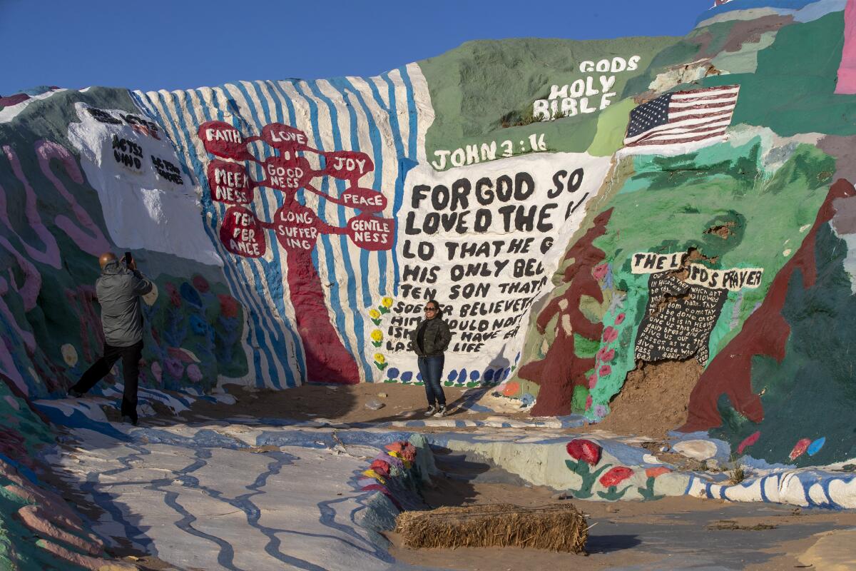 A person stands near a colorful, painted structure in the desert