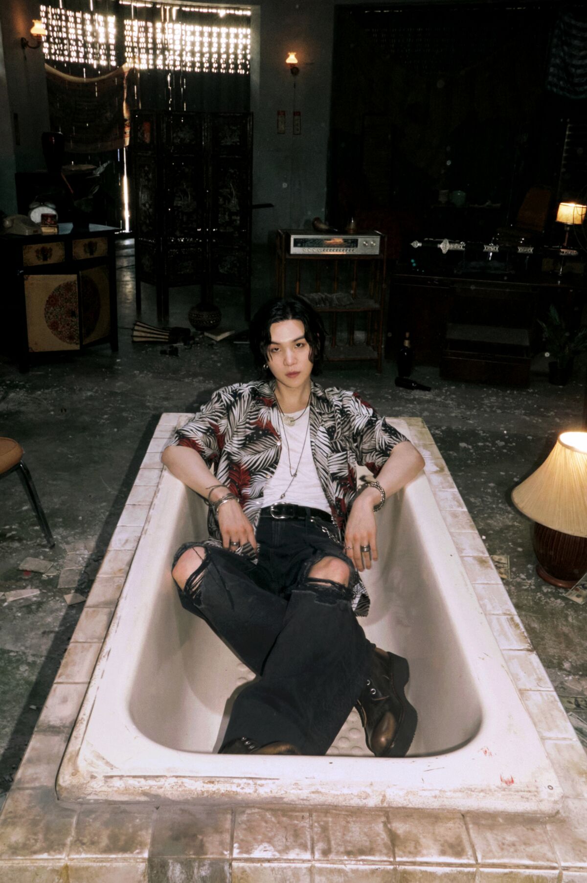 Suga sits in an empty bathtub.