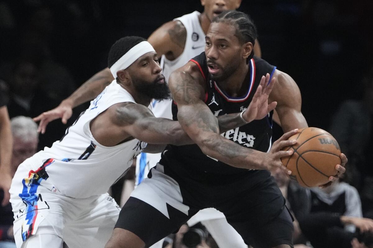 Clippers forward Kawhi Leonard keeps the ball away from the long reach of Nets forward Royce O'Neale.