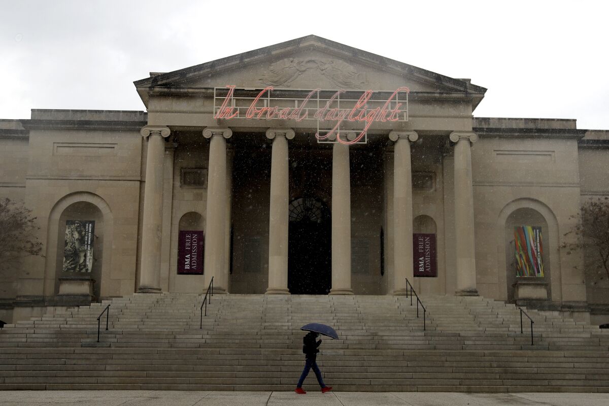 A man holding an umbrella walks past the Baltimore Museum of Art on a rainy, cloudy day.