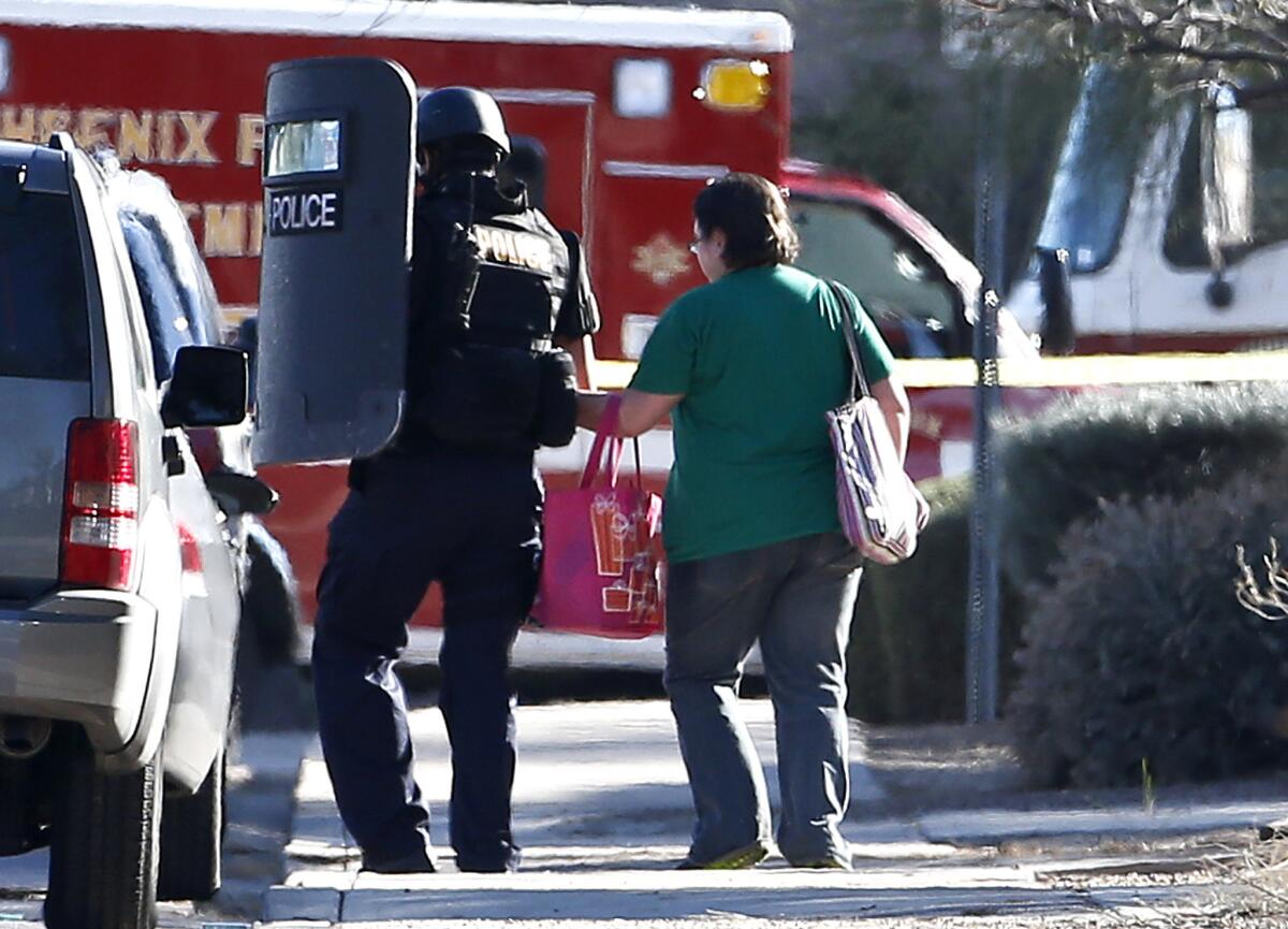 A member of the Phoenix Police Department SWAT team leads a female neighbor to safety as the SWAT team prepares to enter the home of a suspect in the shooting at a Phoenix office building.
