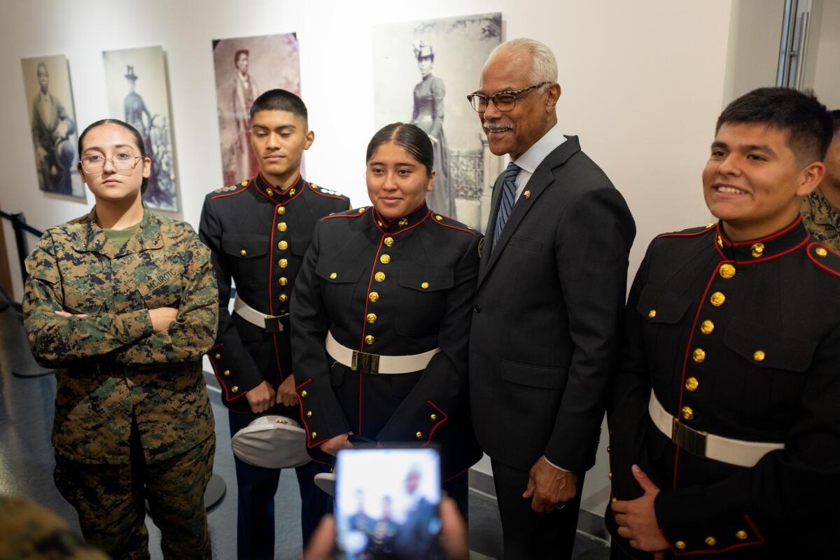 A man in a suit poses for a portrait with four young people, three in Marine Corps dress uniform and one in camouflage.