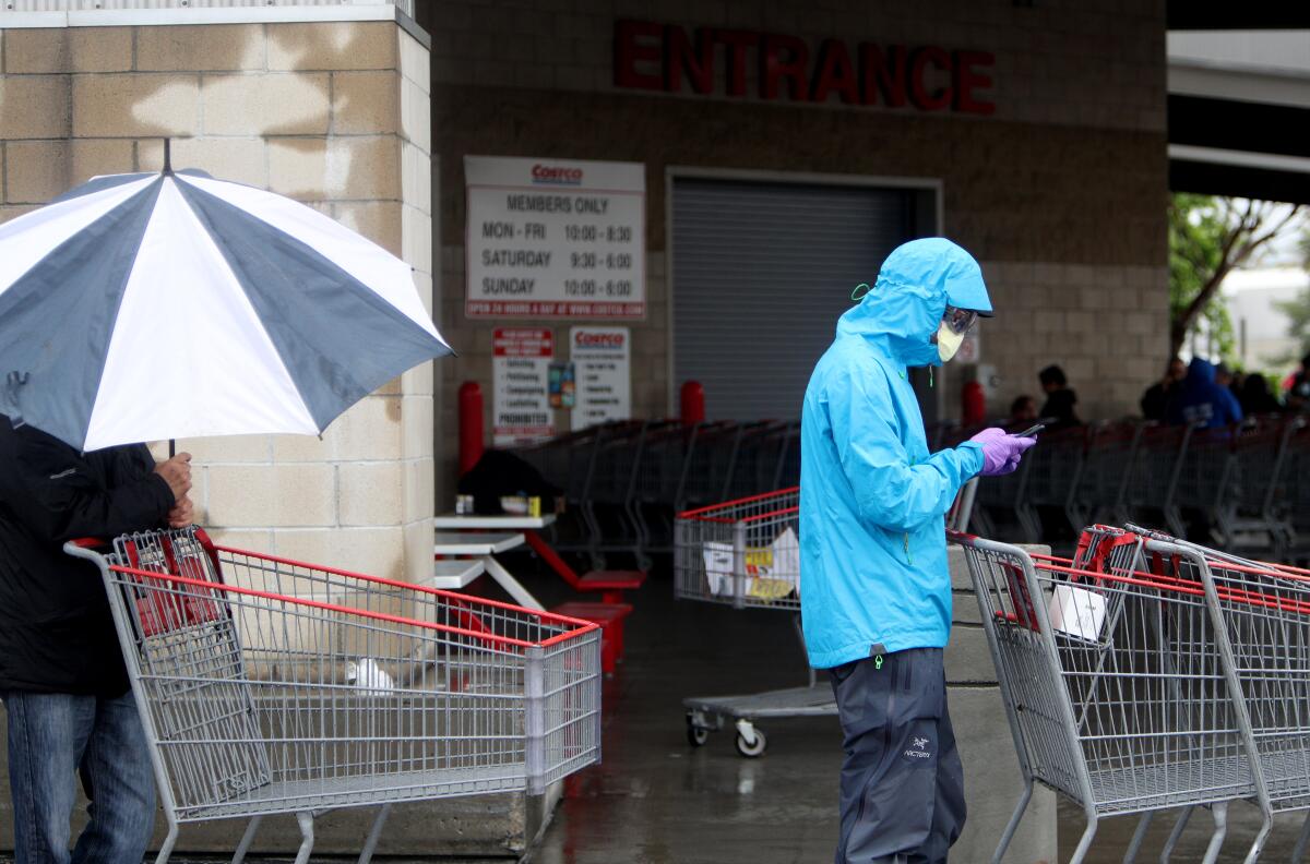 A person wears a mask and gloves while waiting in line at Costco in mid-March. Beginning on Friday, employees and customers at essential businesses such as at the warehouse club will be required to wear masks covering their nose and mouth.