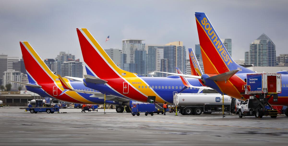 Three passenger jets with Southwest branding sit at airport gates with a city skyline in the background.