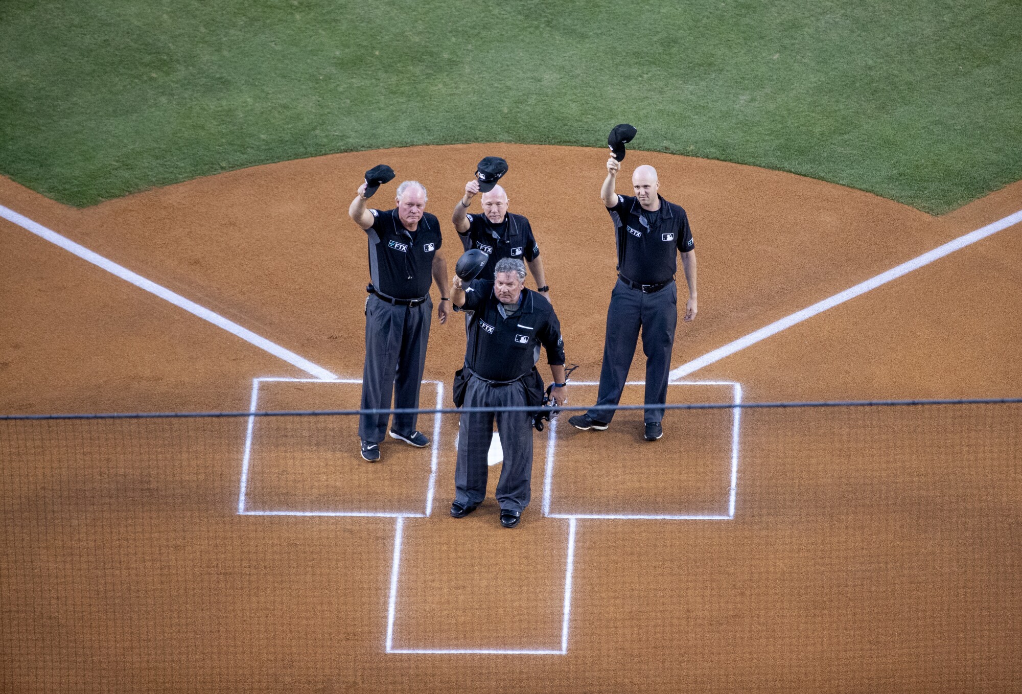 The referees of the game raise baseball caps in front of the press box in honor of Vin Scully. 