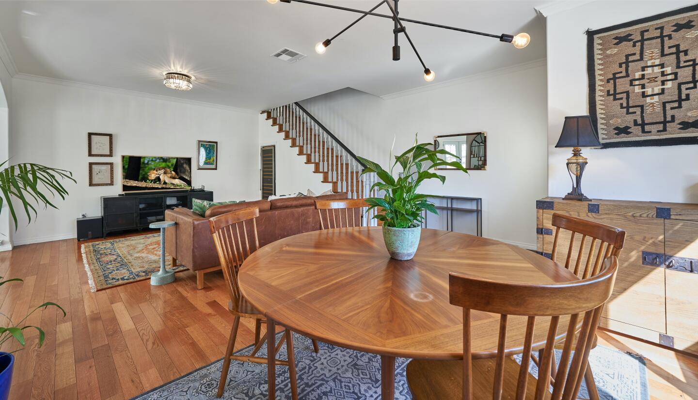 The furnished dining area with light fixtures has a living room and stairs behind it.