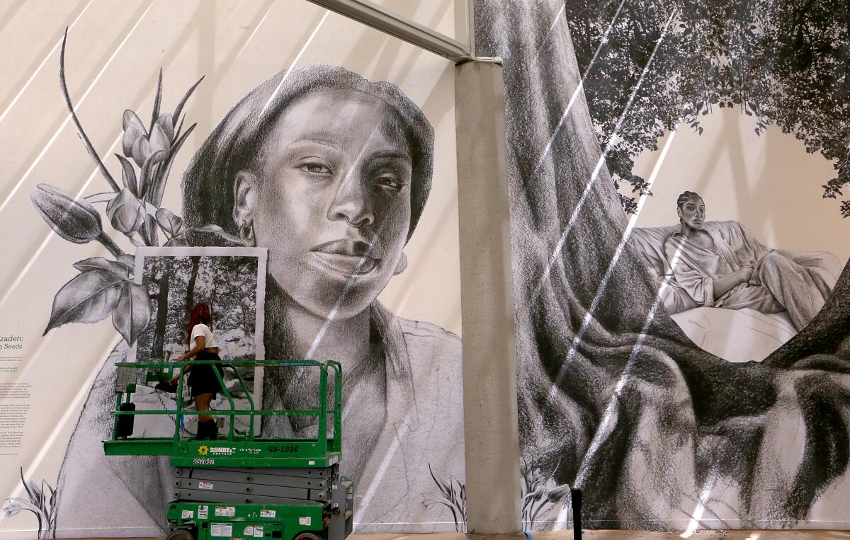Artist Tatyana Fazlalizadeh stands on a cherry picker as she paints a large mural featuring the face of a Black woman