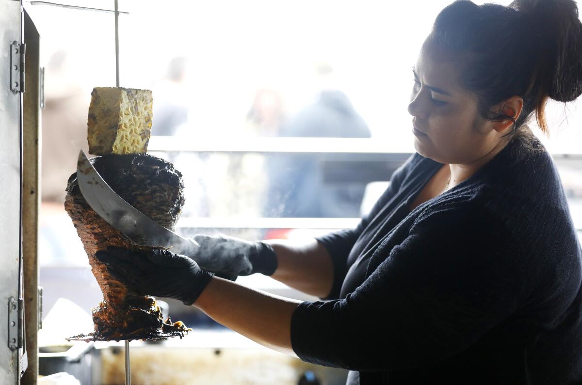 Elvia Huerta, the co-owner and taquera of Evil Cooks, a two-person taco operation with pop ups at various places around Los Angeles, slices meat from the black trompo at Smorgasburg at Row DTLA.