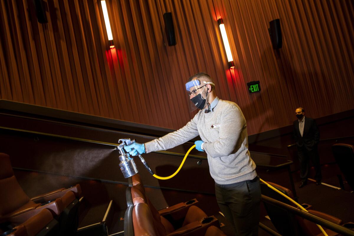 A man wearing a mask and face shield uses an apparatus to sanitize a movie auditorium.