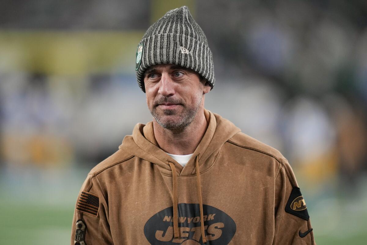Aaron Rodgers wears a beanie and sweater on the field before a football game.