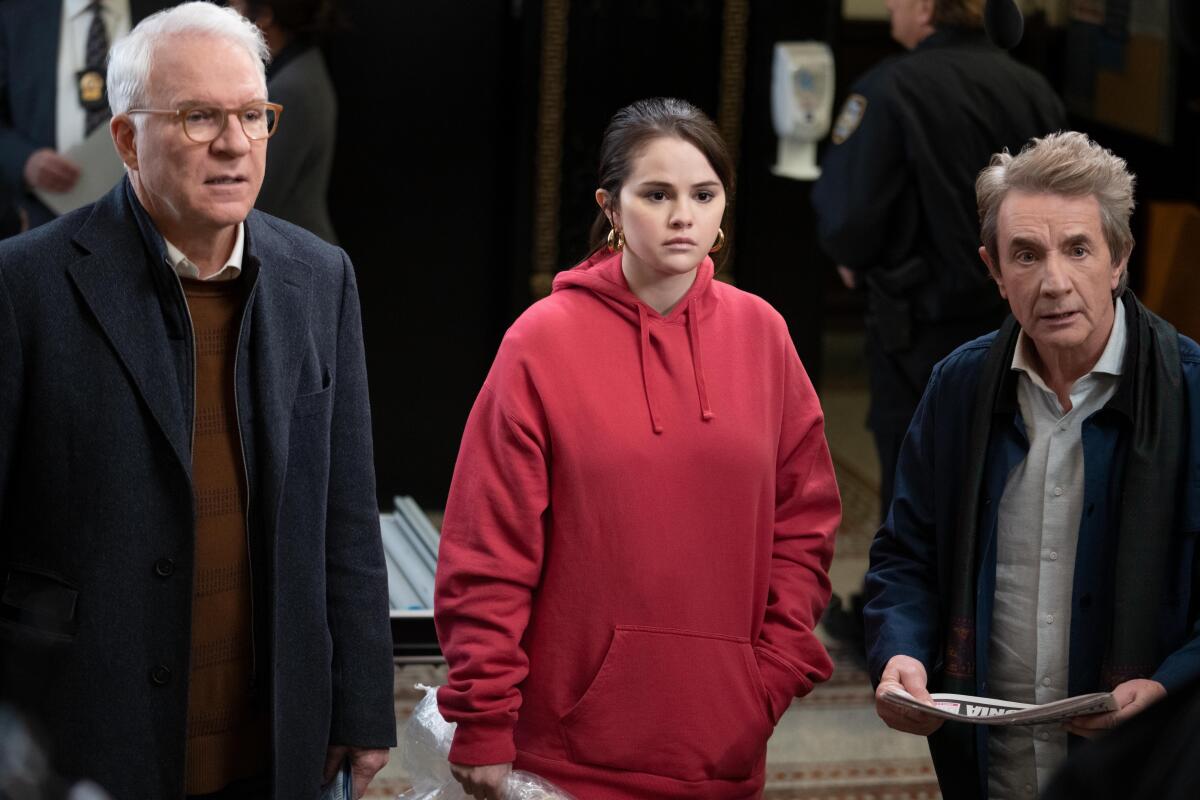 Two older men flank a young woman in a red hoodie.