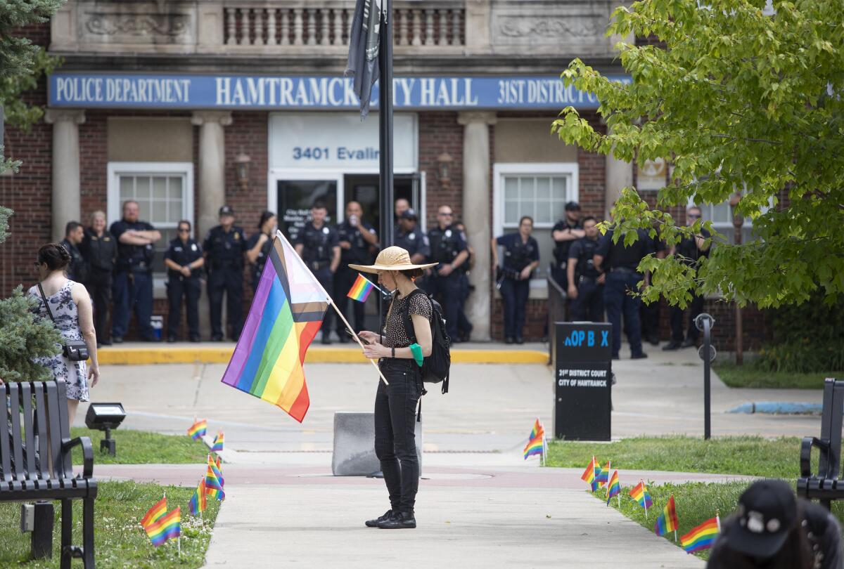 A person holds an LGBTQ+ pride flag outside Hamtramck, Mich., City Hall as police stand near the door.