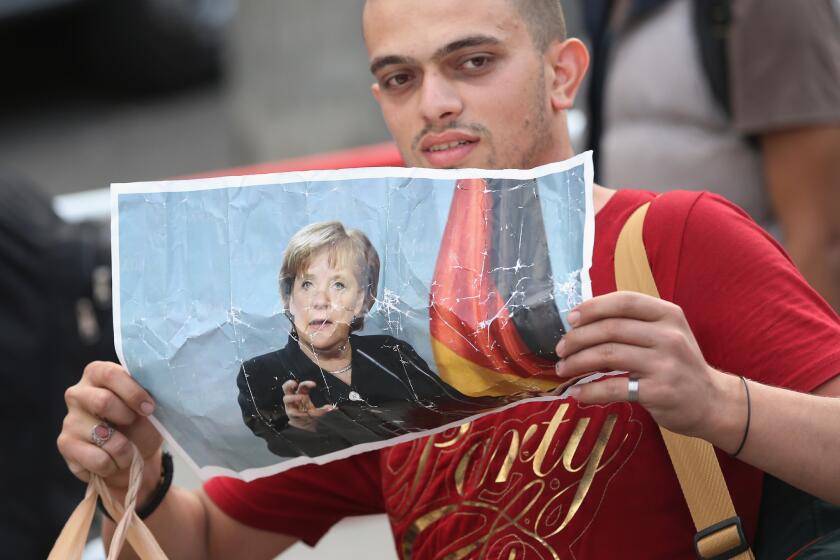 A migrant from Syria holds a picture of German Chancellor Angela Merkel as he arrives from Hungary at Munich's main railway station on Sept. 5. Germany has agreed to set aside more than $6 billion next year to help migrants.