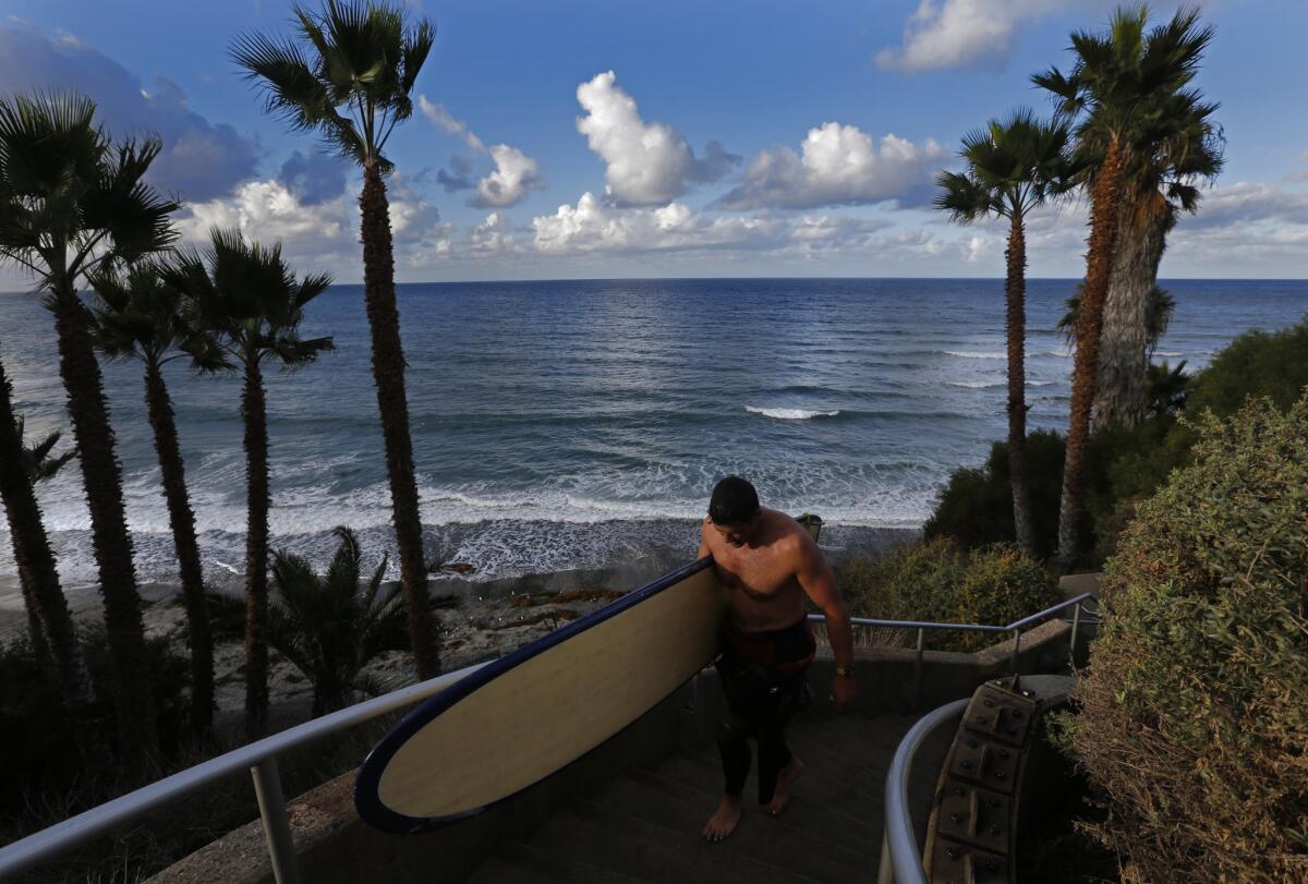 Dr. Johnny Greenfield carries his surfboard up from Swami's beach in Encinitas, where two surfers died recently at the well-known north San Diego County spot.