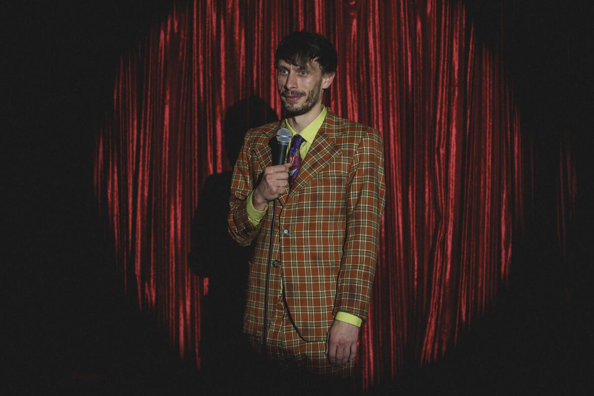 A man in a plaid suit performs onstage.