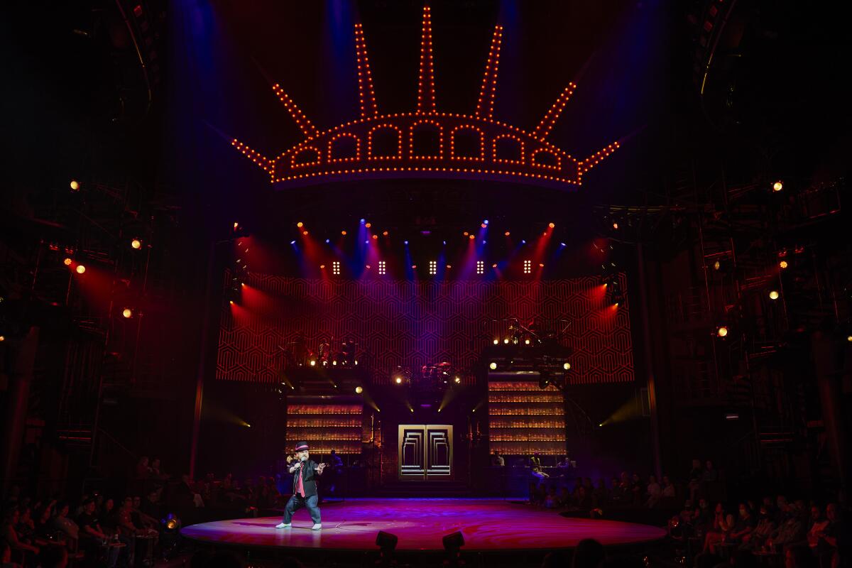 A comedian on a big stage in Las Vegas with lights in the shape of the Statue of Liberty's crown