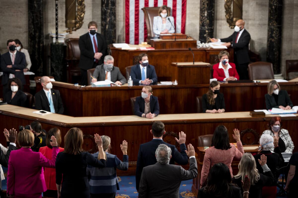 Nancy Pelosi sits at a desk in the House chamber; members of Congress stand holding up their right hands.