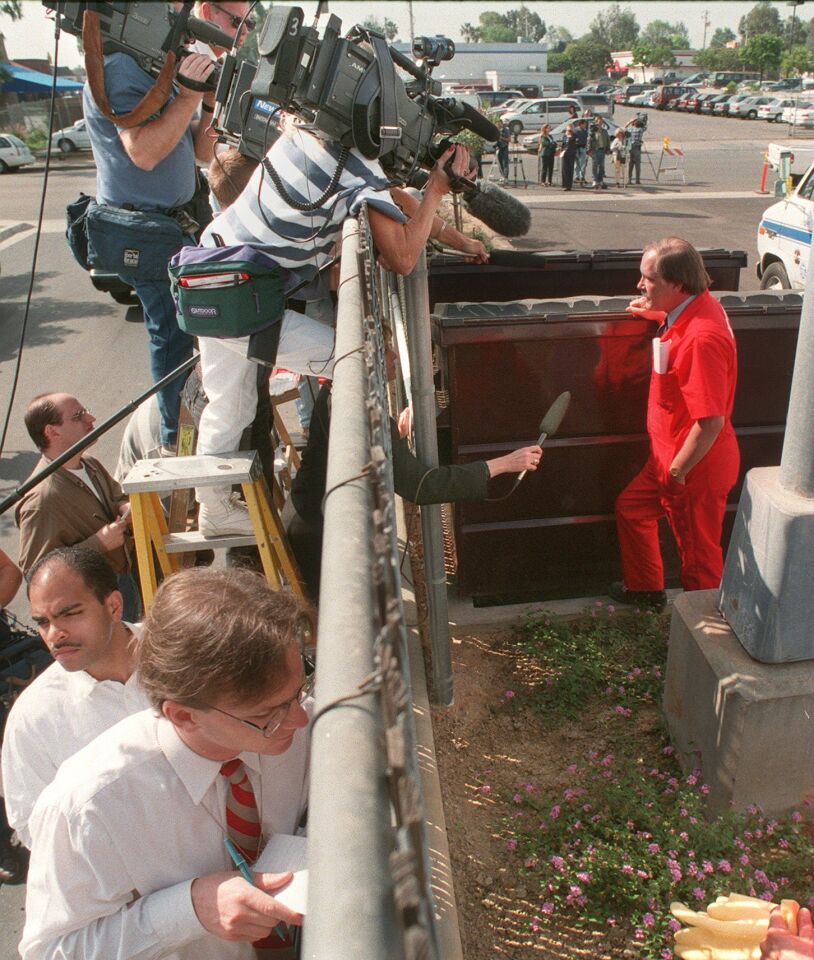 Leaning over and poking their arms through a fence, reporters interview Deputy Investigator George Dicka of the San Diego County Medical Examiner's Office on March 27, 1997, the day after the Heaven's Gate mass suicide was discovered in Rancho Santa Fe.
