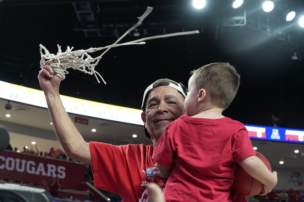 Houston coach Kelvin Sampson cuts down the net while holding his grandson Kylen Sampson, in celebration of Houston winning the American Athletic Conference regular-season championship, following the team's NCAA college basketball game against Wichita State, Thursday, March 2, 2023, in Houston. (AP Photo/Kevin M. Cox)