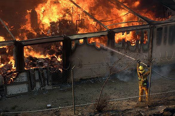 A firefighter pours water on a structure at the Sky Terrace Mobile Lodge in Lake View Terrace as the Marek fire in Southern California grew to 3,700 acres, fanned by high wnds.