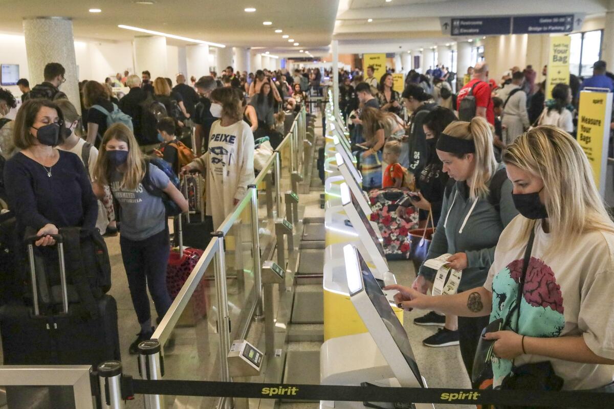 Passengers check themselves in at kiosks and others stand in line at a busy airport.