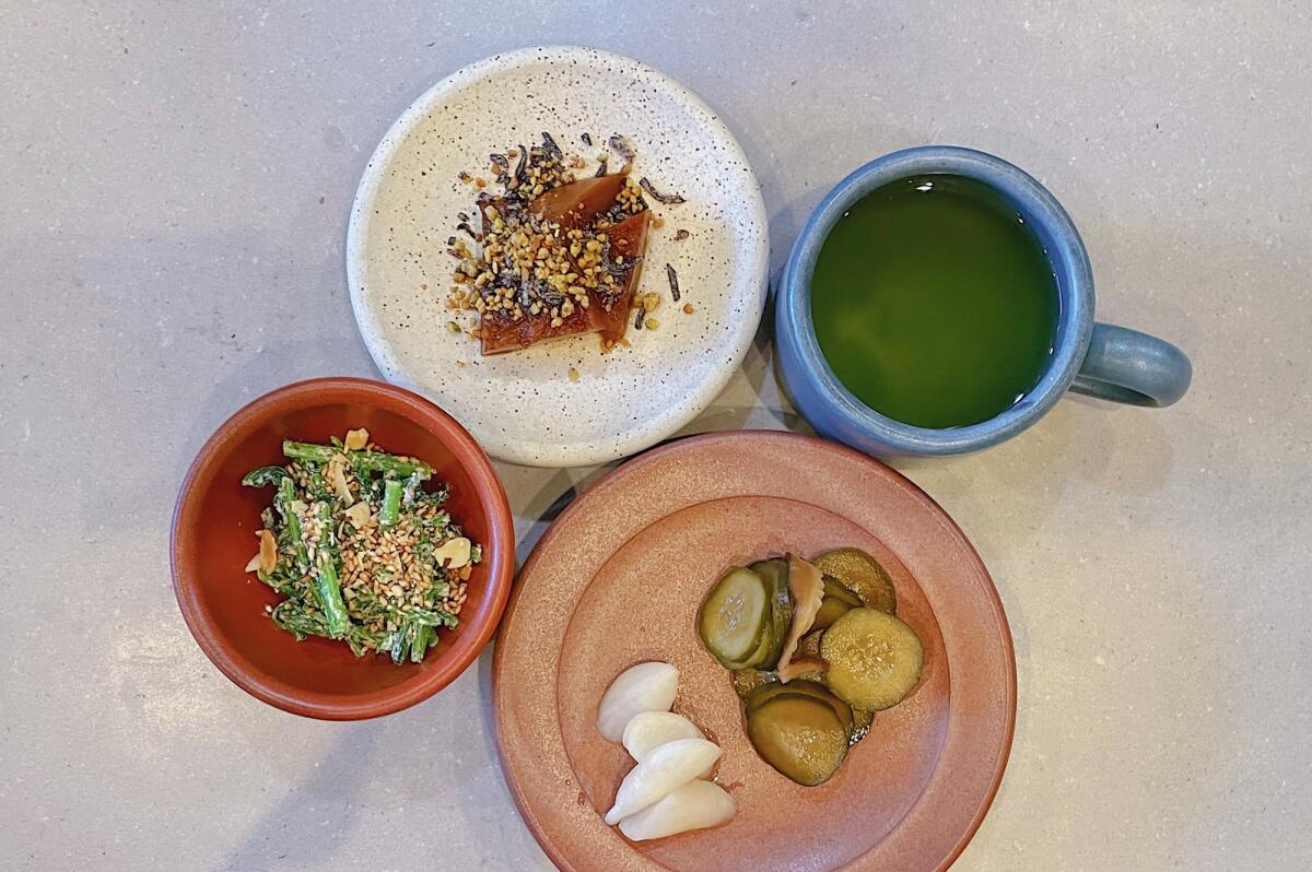 An overhead photo of a trio of plates from Konbi Ni's new Japanese breakfast, including pickles, greens and squash.