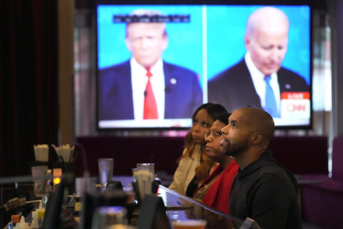Three people watch the presidential debate in a room in a Chicago neighborhood.