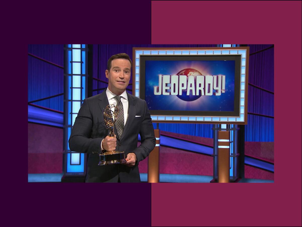 a man stands holding an Emmy statue on the set of Jeopardy