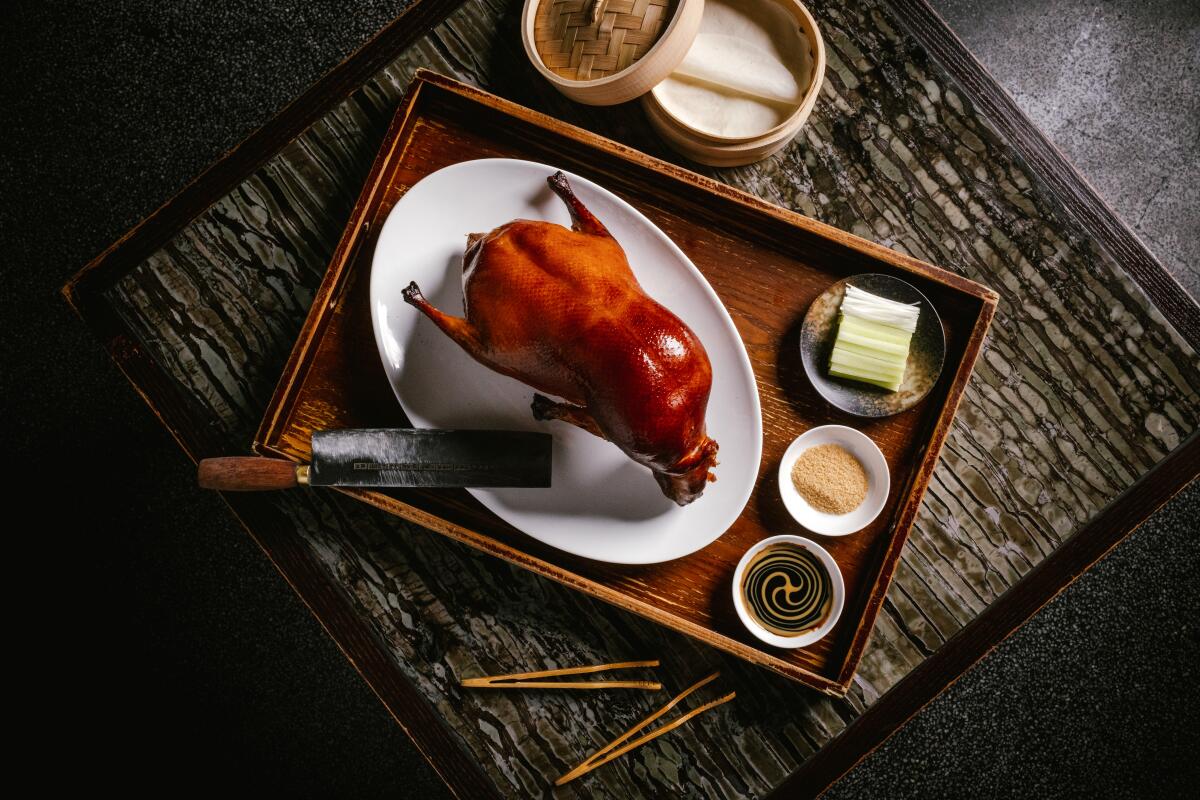 Applewood Roasted Peking Duck on a wood tray with various sauces next to pancakes in a steamer basket