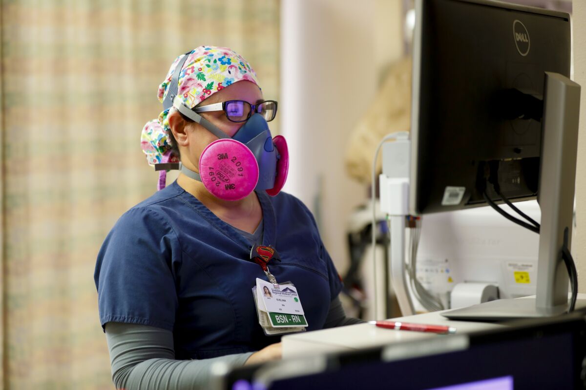 An RN wears a half face mask fitted with a P100 filter while updating a patient’s chart.