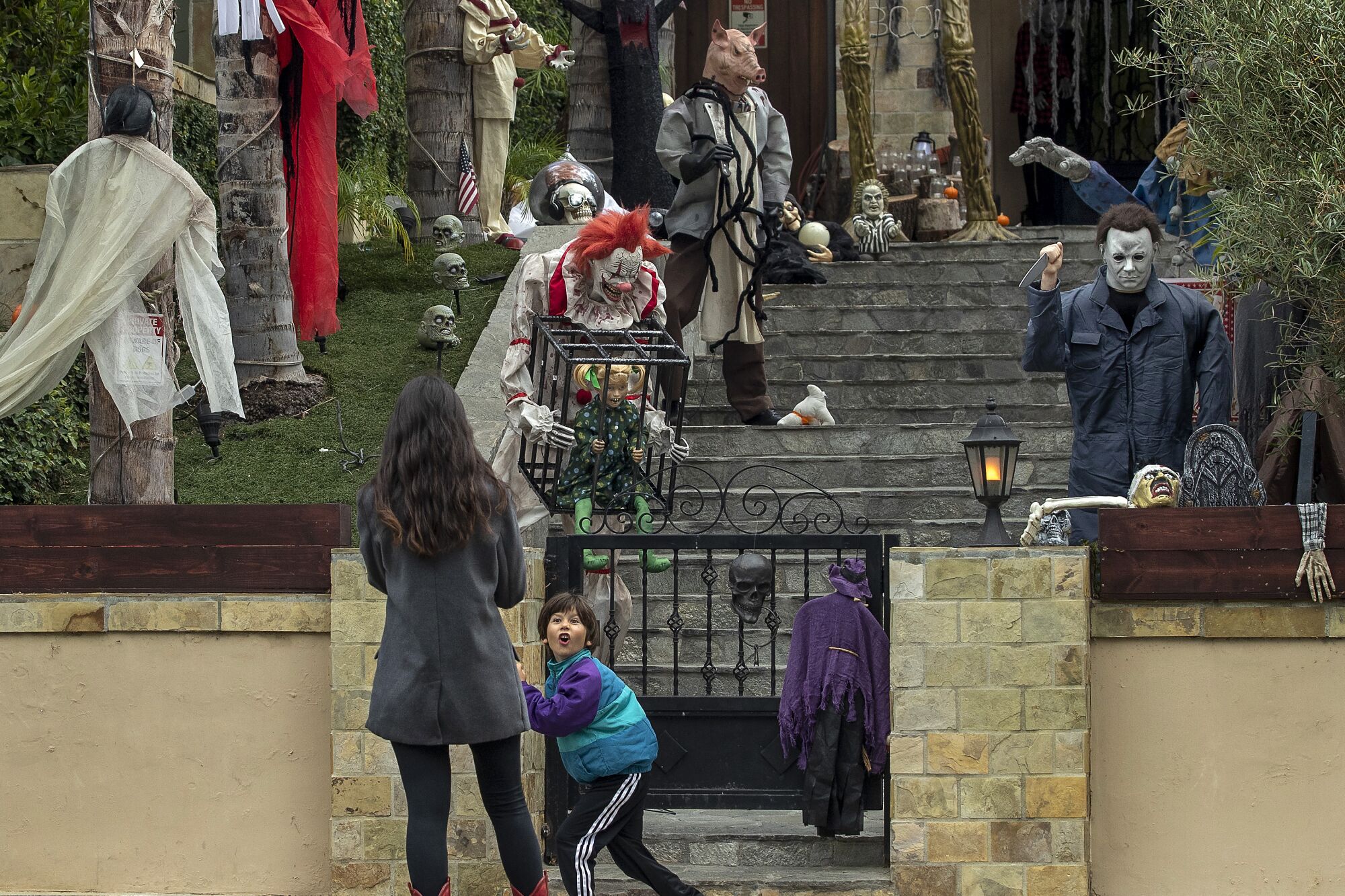 A boy turns around to make a scary face at his mother outside a home decorated with ghoulish creatures