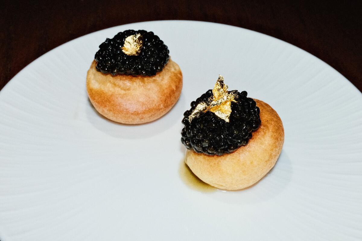 Two caviar- and gold-topped gougères on a white plate at West Hollywood restaurant Chez Mia