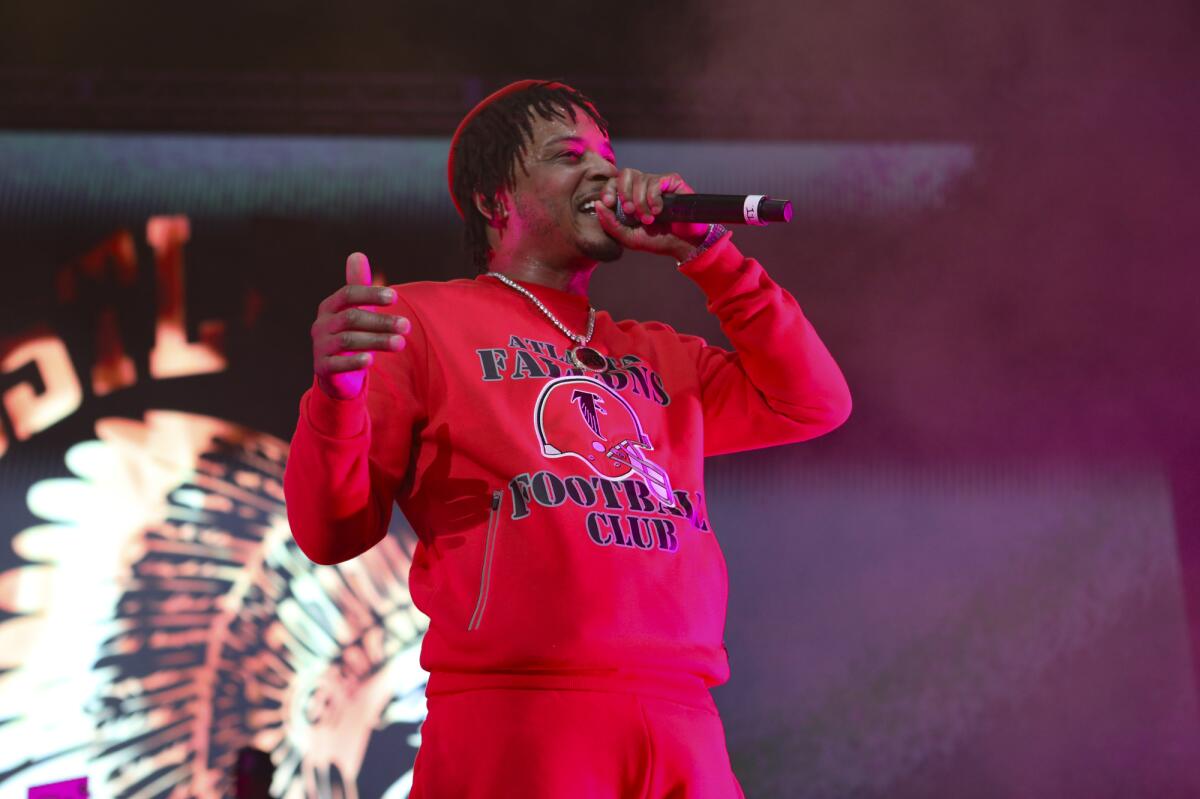 Man in a red sweater and red sweatpants raps into a microphone while onstage