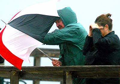 Storm-watchers on the Seal Beach pier struggle with their umbrella after a wind-driven rain storm hit the area.