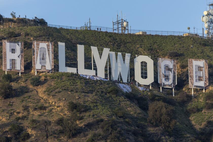 Hollywood, CA - February 14: Workers install letters to cover the Hollywood sign to eventually read 'RAMS HOUSE' Monday, Feb. 14, 2022 in Hollywood, CA. (Brian van der Brug / Los Angeles Times)