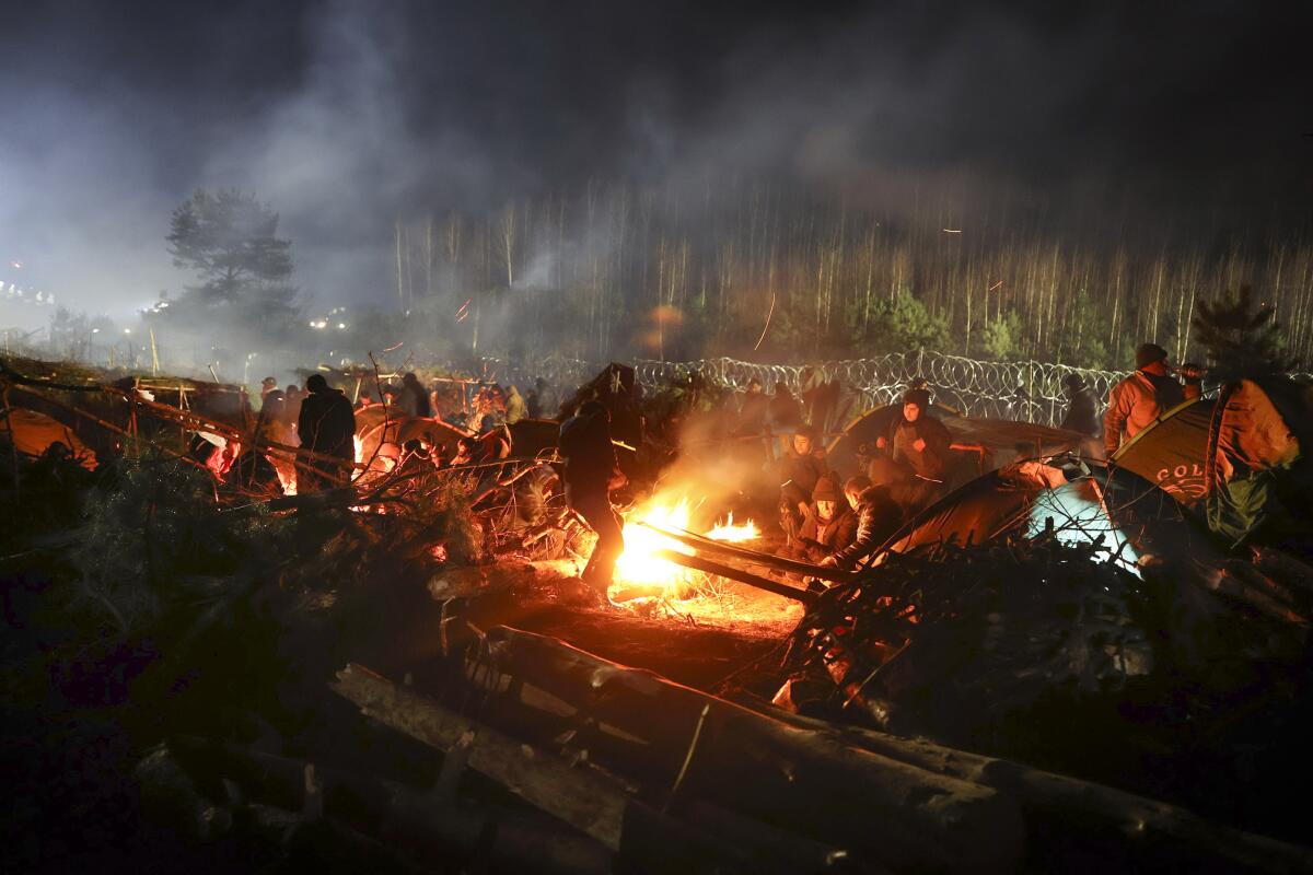 Migrants warming themselves at a fire in a forest