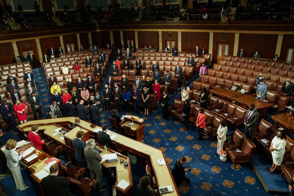 Lawmakers wearing masks, some socially distanced, stand in the U.S. House, with Nancy Pelosi at the podium.