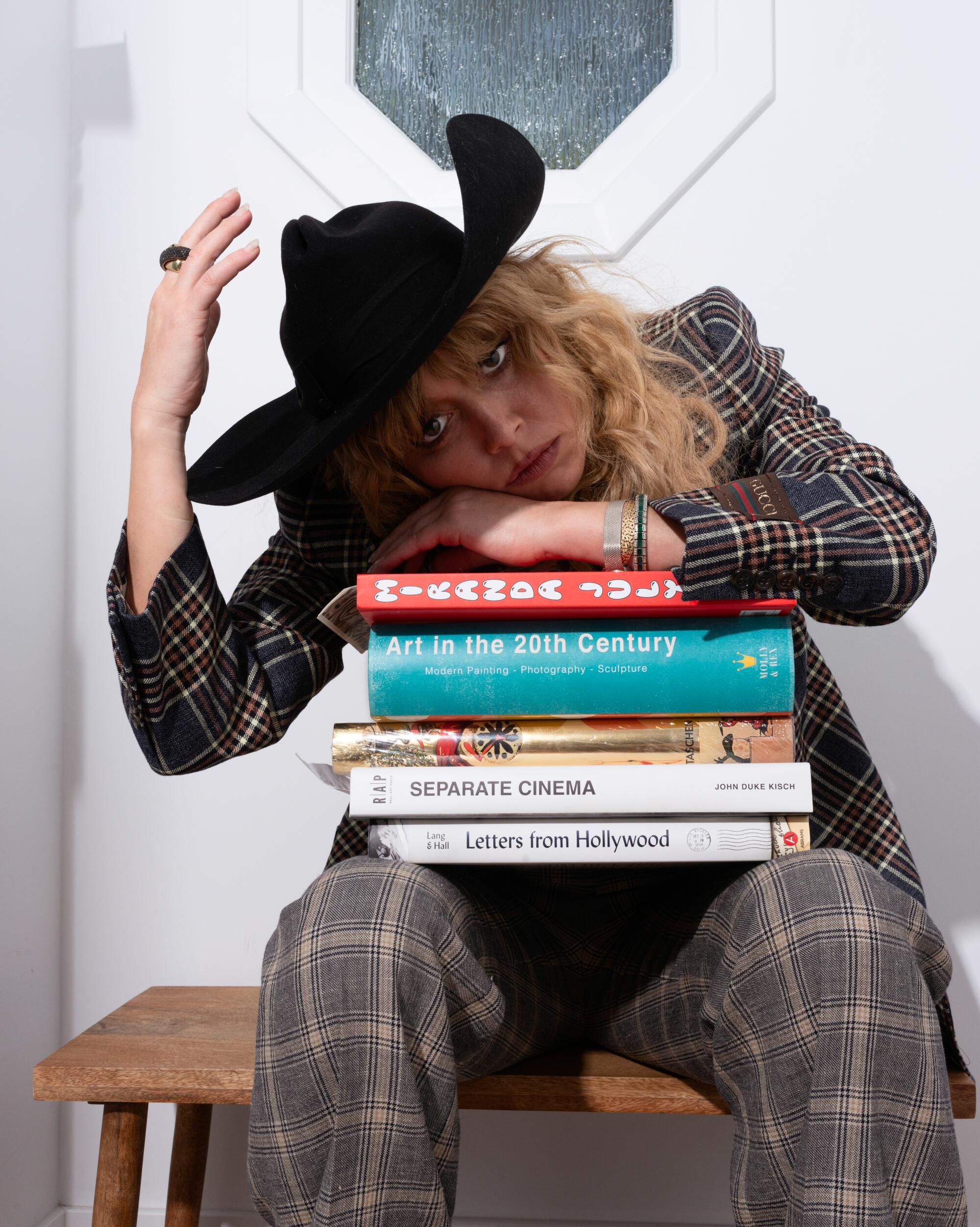 A woman rests her head on a stack of books while reaching up for her cowboy hat
