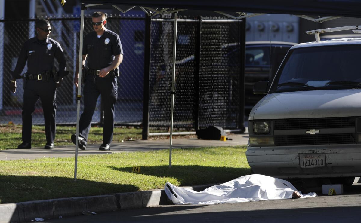 LAPD officers walk by a body in front of Woodbine Park in the Palms area of Los Angeles. Two shootings left one person dead and at least three others wounded.