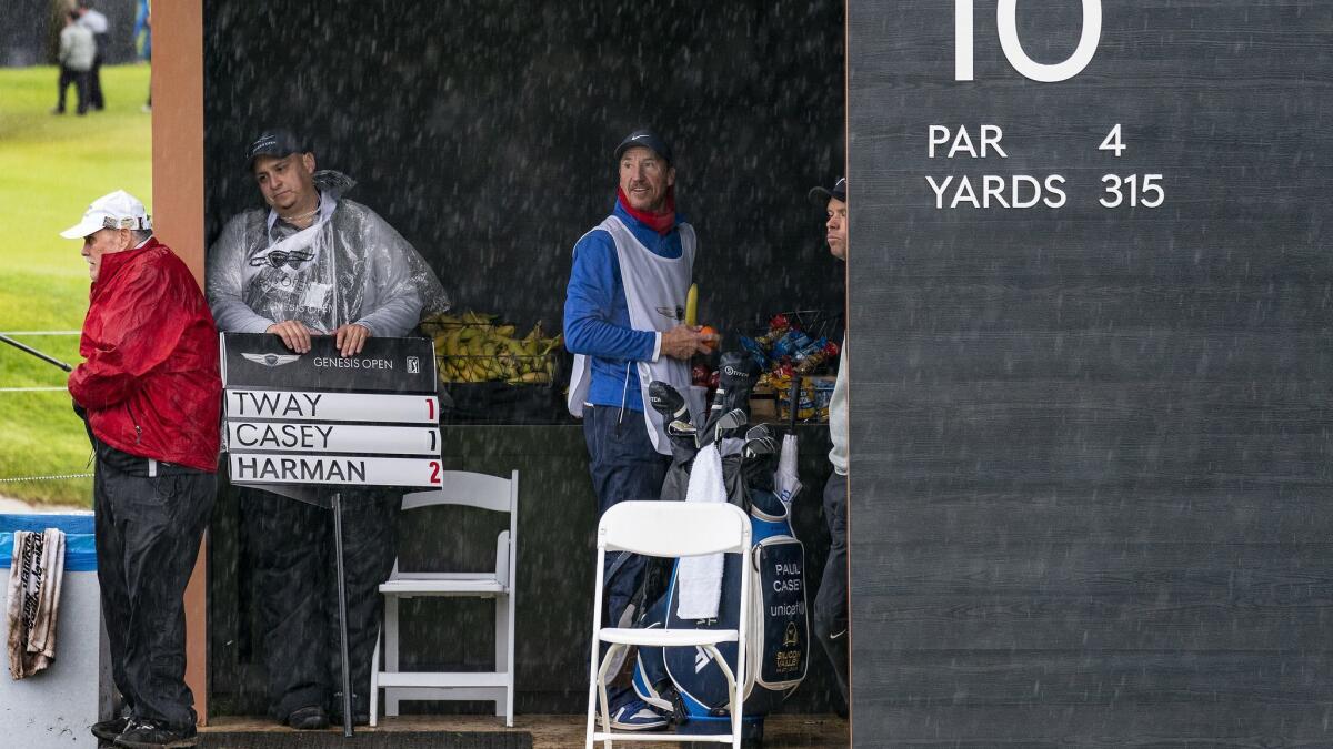 The sign guy takes refuge with the caddies in a snack hut at the 10th tee during a downpour in the first round of the Genesis Open at Riviera Country Club on Thursday in Pacific Palisades. Play was suspended for more than six hours due to rain.