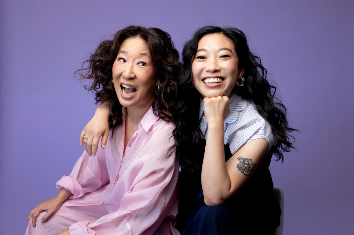 Two Asian American women smile as one drapes her arm around the other's shoulder for a portrait.