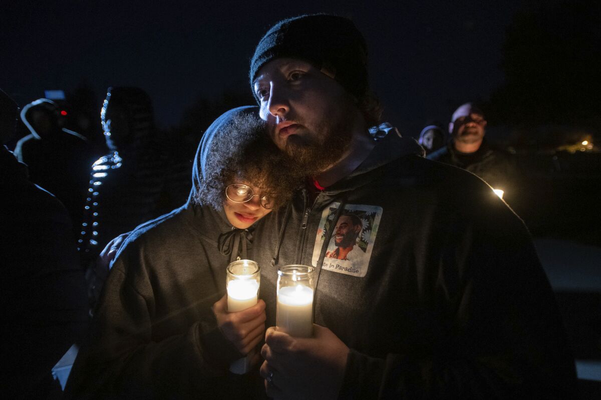 Candlelight illuminates a photo of Tyre Nichols on the hoodie worn by a mourner, who comforts another mourner.