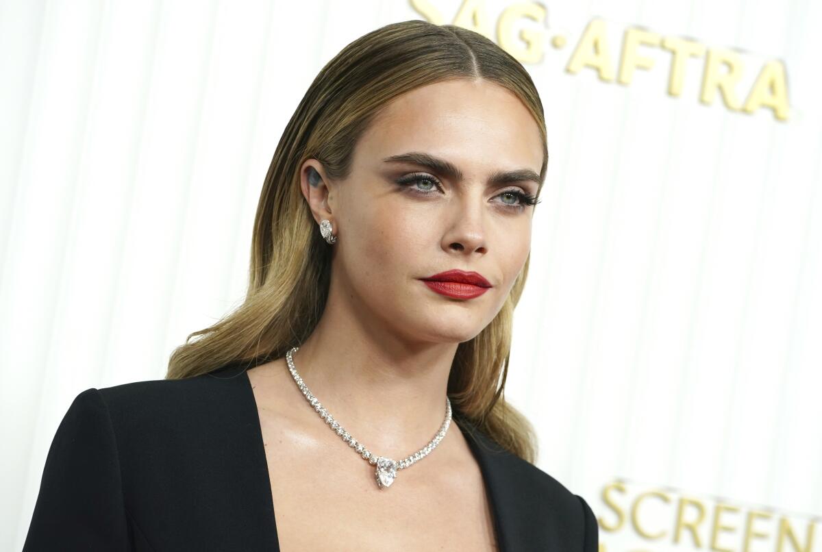Cara Delevingne, dressed in black with a diamond necklace, poses for cameras. 