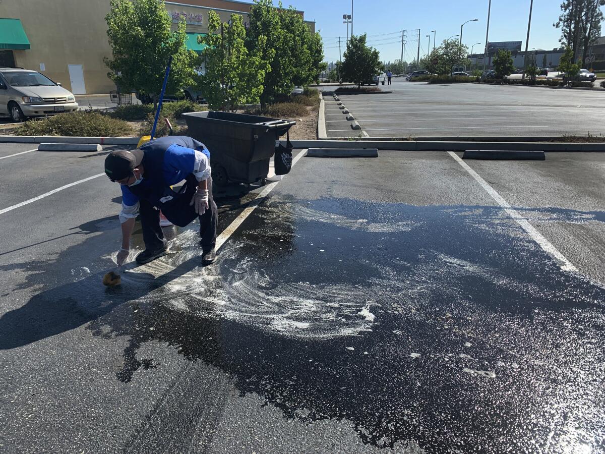 A man scrubs the blood stains left over from a July 9 robbery and pistol-whipping in a Rowland Heights shopping plaza