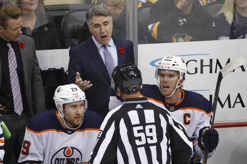 Edmonton Oilers head coach Dave Tippett stands behind Connor McDavid (97) and Leon Draisaitl (29) as he talks with linesman Steve Barton (59) during the first period of an NHL hockey game against the Pittsburgh Penguins in Pittsburgh, Saturday, Nov. 2, 2019. The Oilers won 2-1 in overtime on a goal by Draisaitl. (AP Photo/Gene J. Puskar)