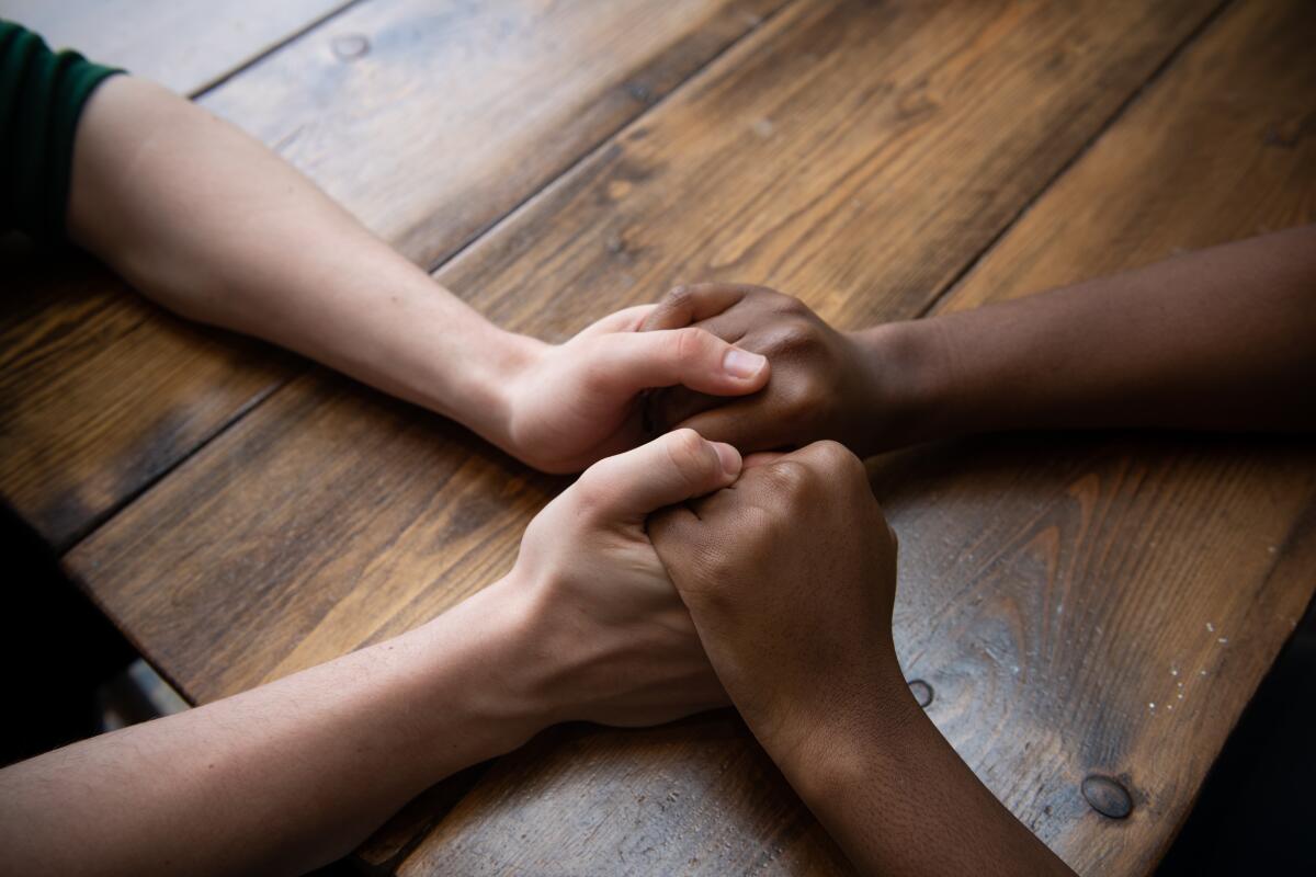 Close-up of two people holding hands at a wooden kitchen table